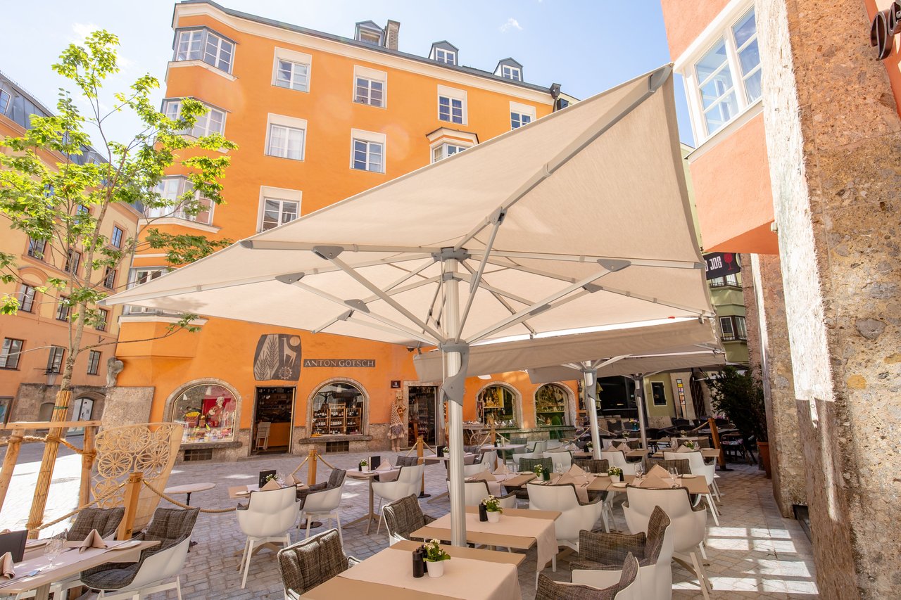 Großer Mittelstockschirm beschattet eine Restaurantterrasse mit gedeckten Tischen