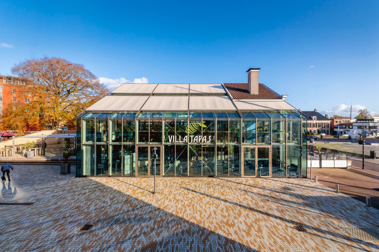 markilux 8800 Aufglasmarkisen auf dem Glasdach des Restaurants Villa Tapas an einem sonnigen Stadtplatz.