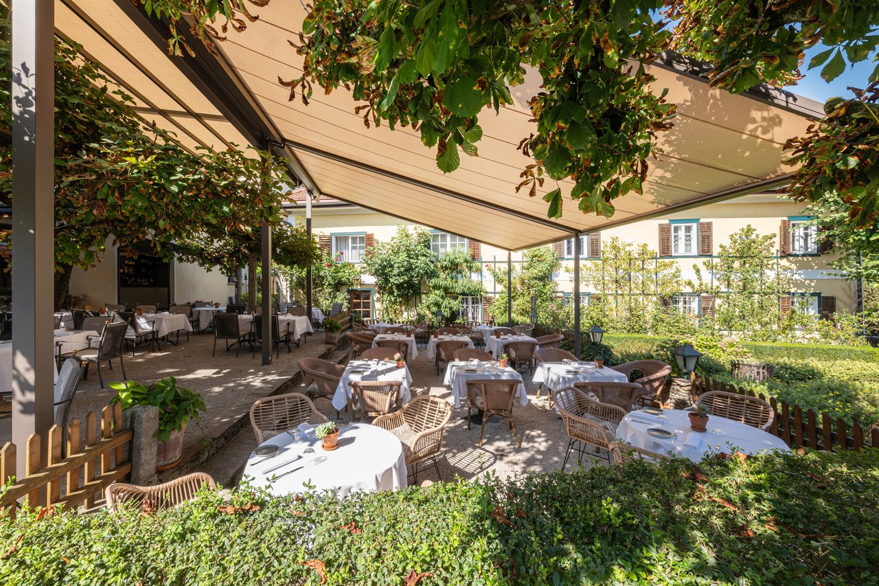 Große markilux pergola stretch überdacht die Gartenterrasse eines Restaurants mit weiß eingedeckten Tischen unter Bäumen.