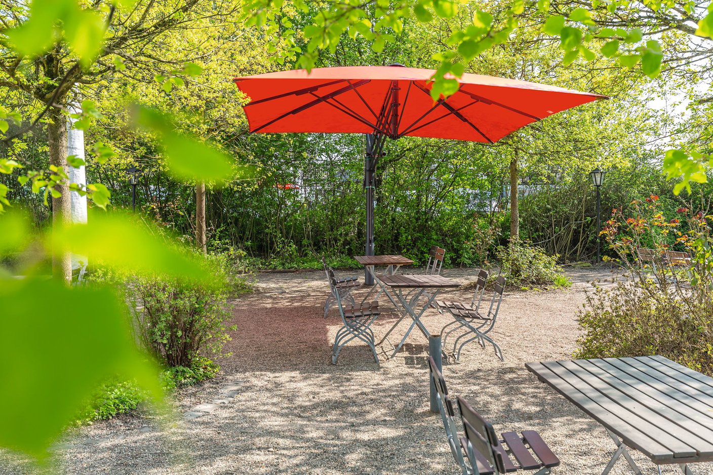 Roter Bahama Sonnenschirm in einem grünen Gastgarten, Laub in der Unschärfe
