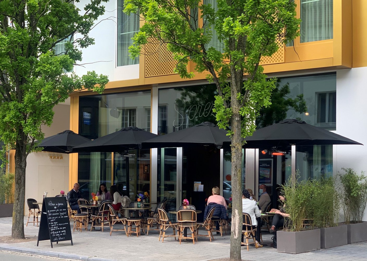 Prostor P6 in Schwarz über der Bestuhlung eines Straßencafés vor einem modernen Gebäude