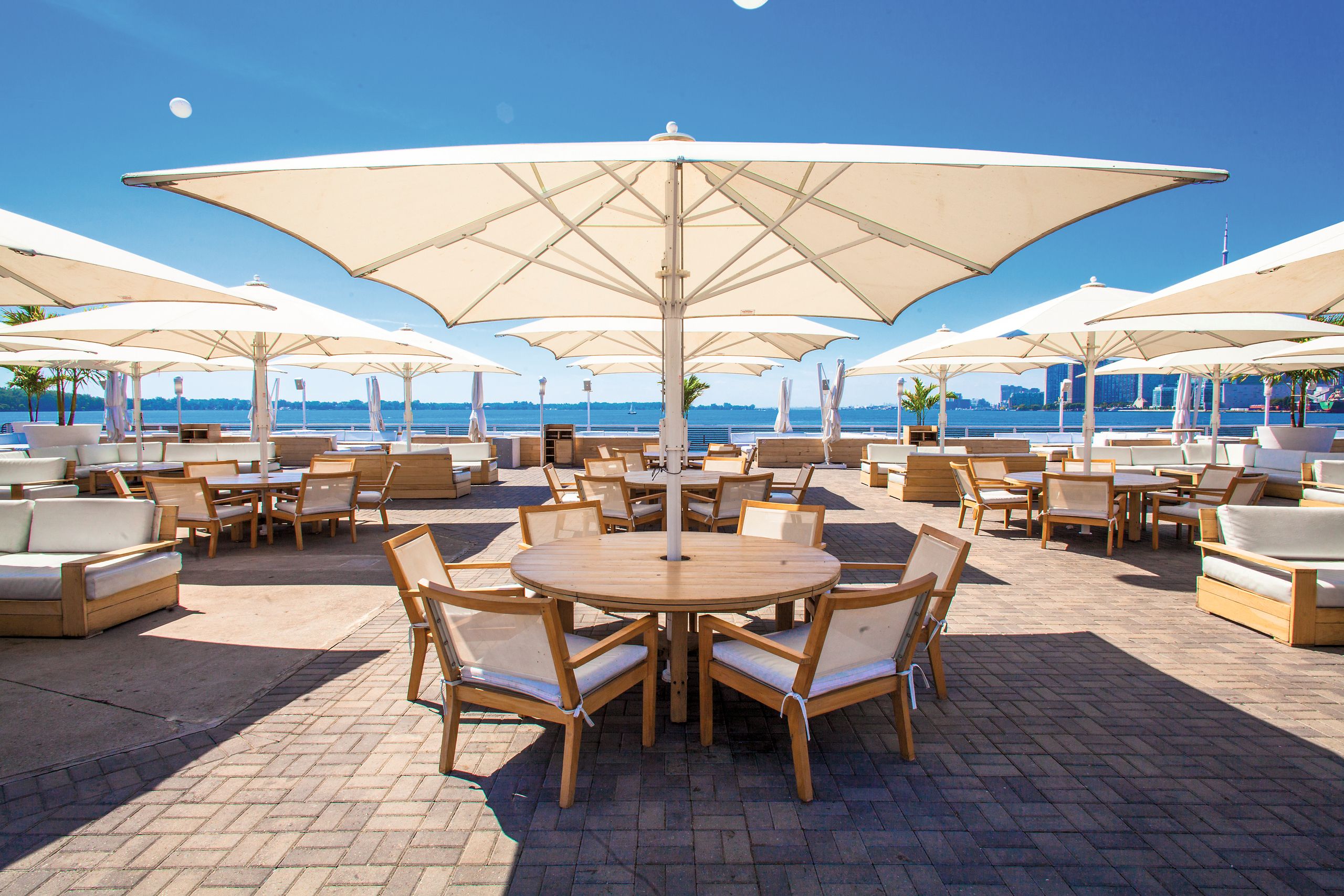 Beige Bahama Jumbrella Großschirme auf einer Dachterrasse mit Seeblick und Loungemöbeln
