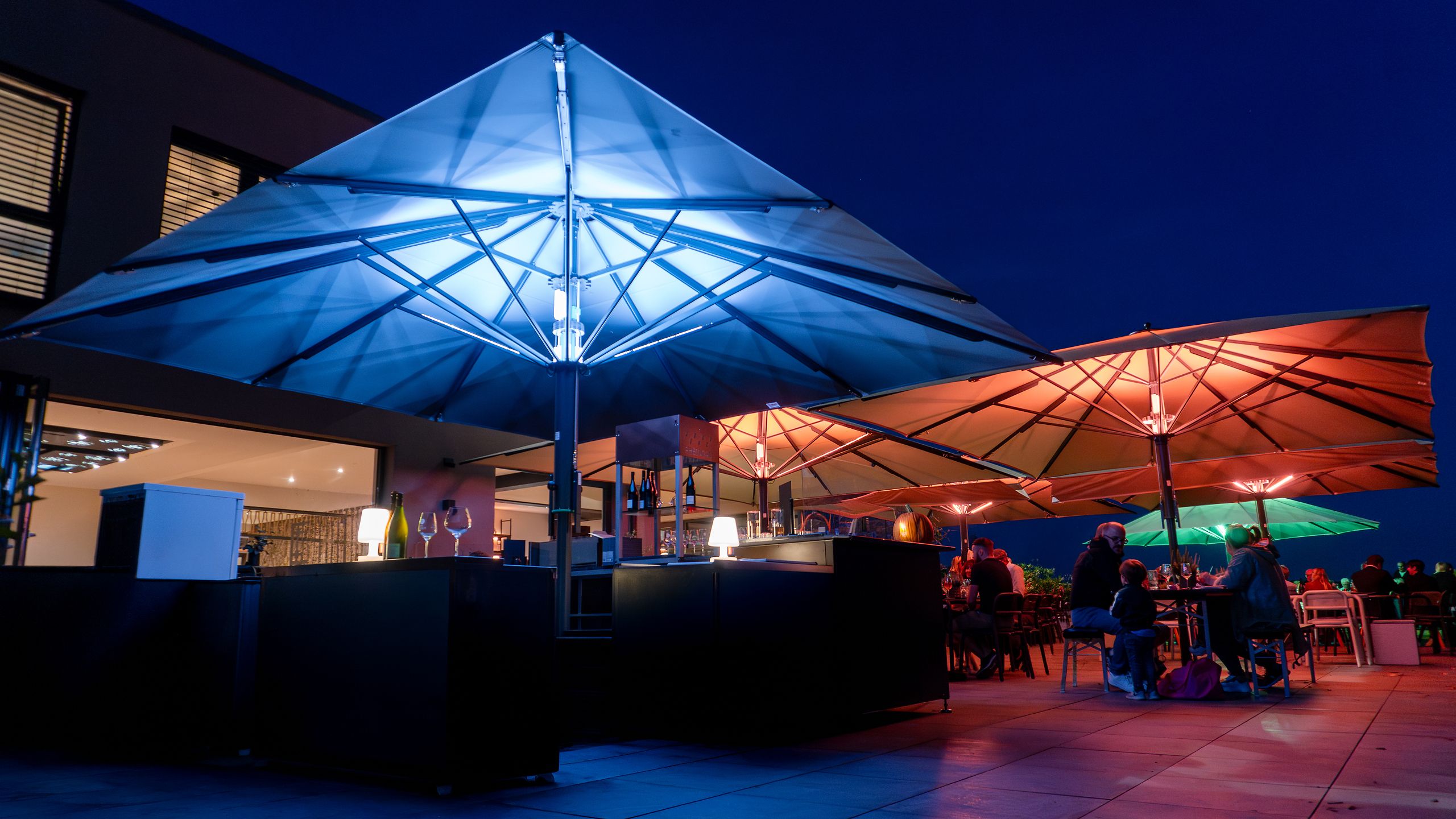 Bahama Jumbrella Großschirme mit farbiger LED-Beleuchtung am Abend über einer Eventfläche