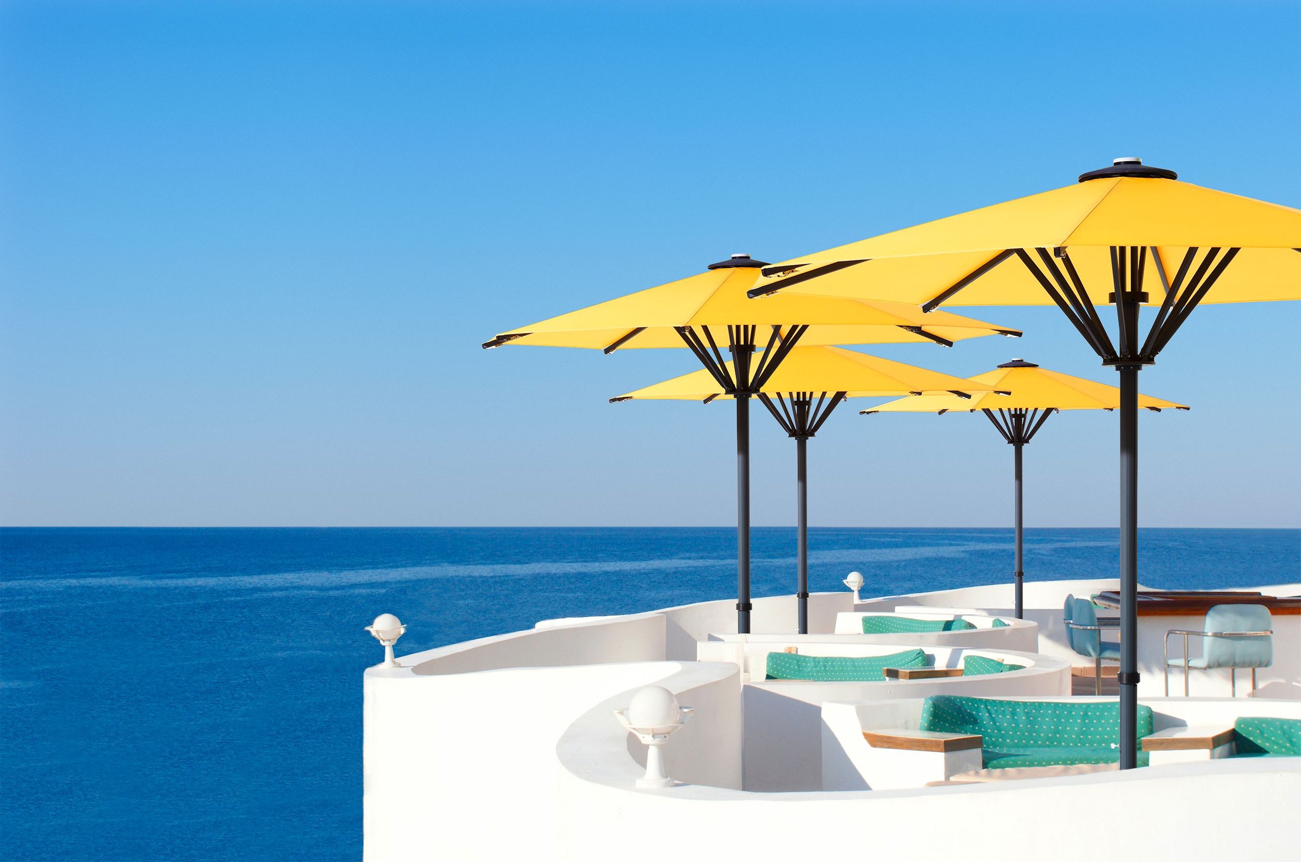 Gelbe runde Bahama Pure Gartenschirme auf einer weißen Terrasse über dem Meer
