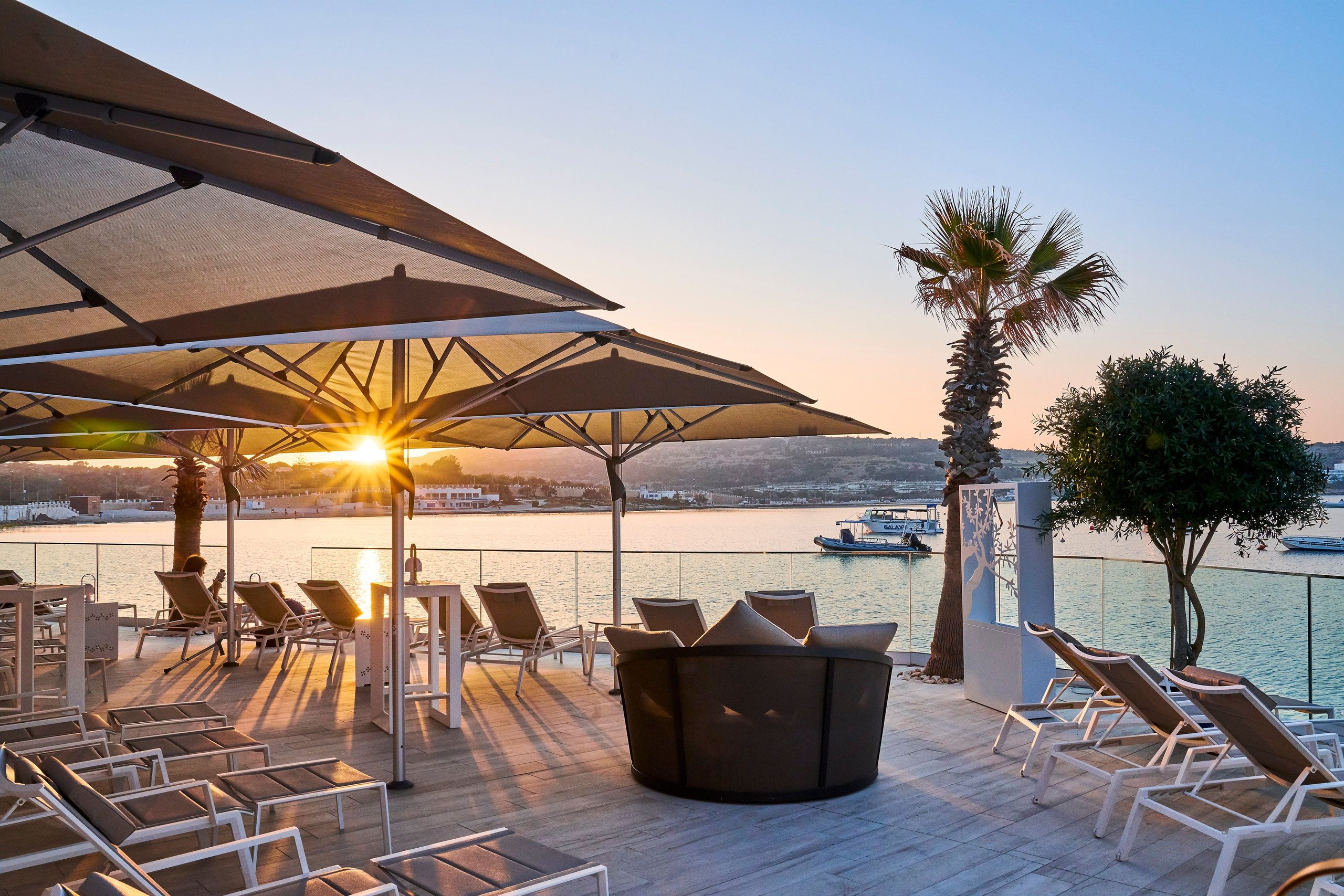 Glatz Fortello über Sonnenliegen einer Beachclub-Terrasse mit Meerblick im Abendlicht