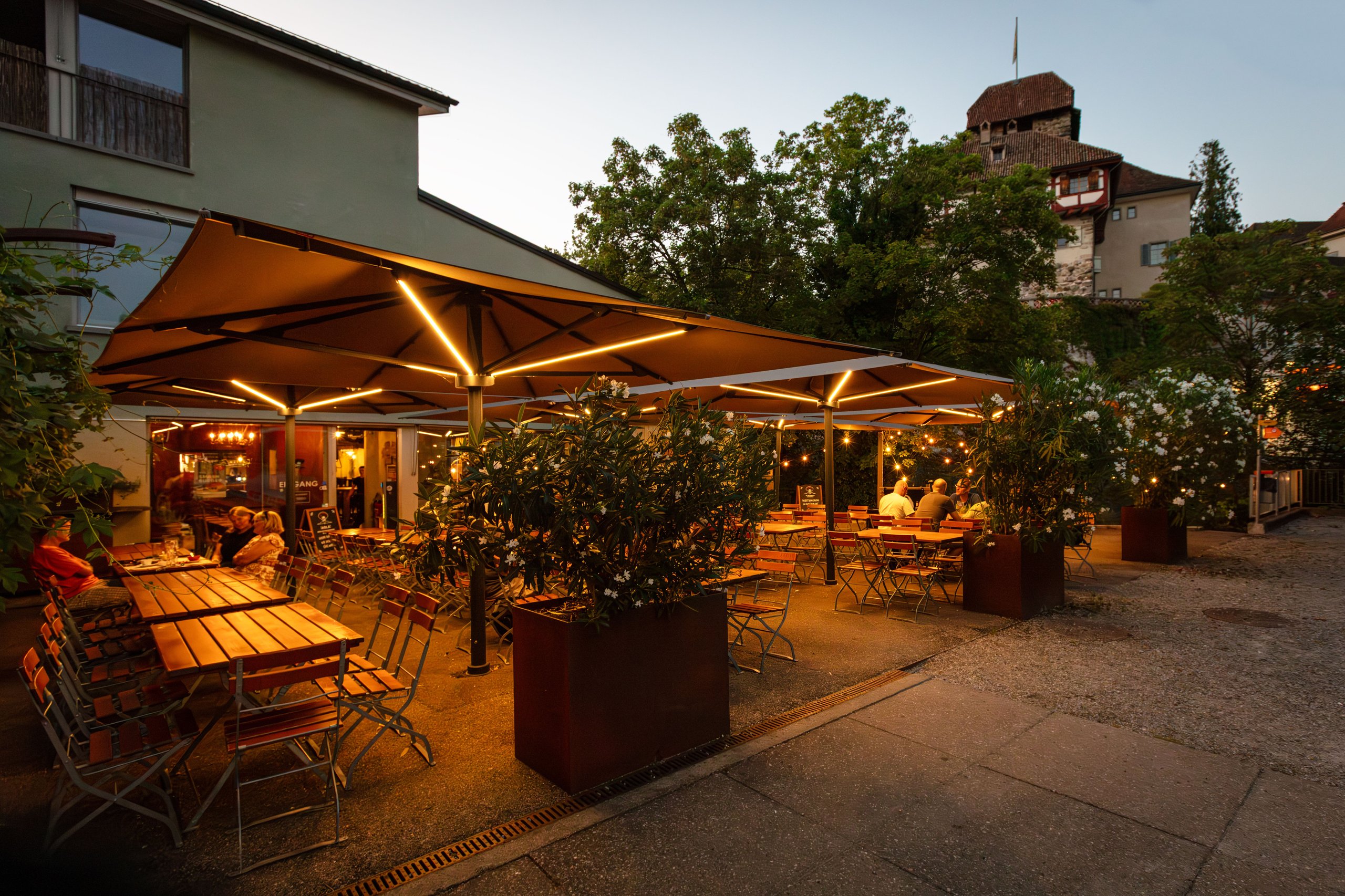 Cremefarbene Palazzo-Noblesse-Schirme mit warmer LED im Burghof des US-MEX in Frauenfeld am Abend