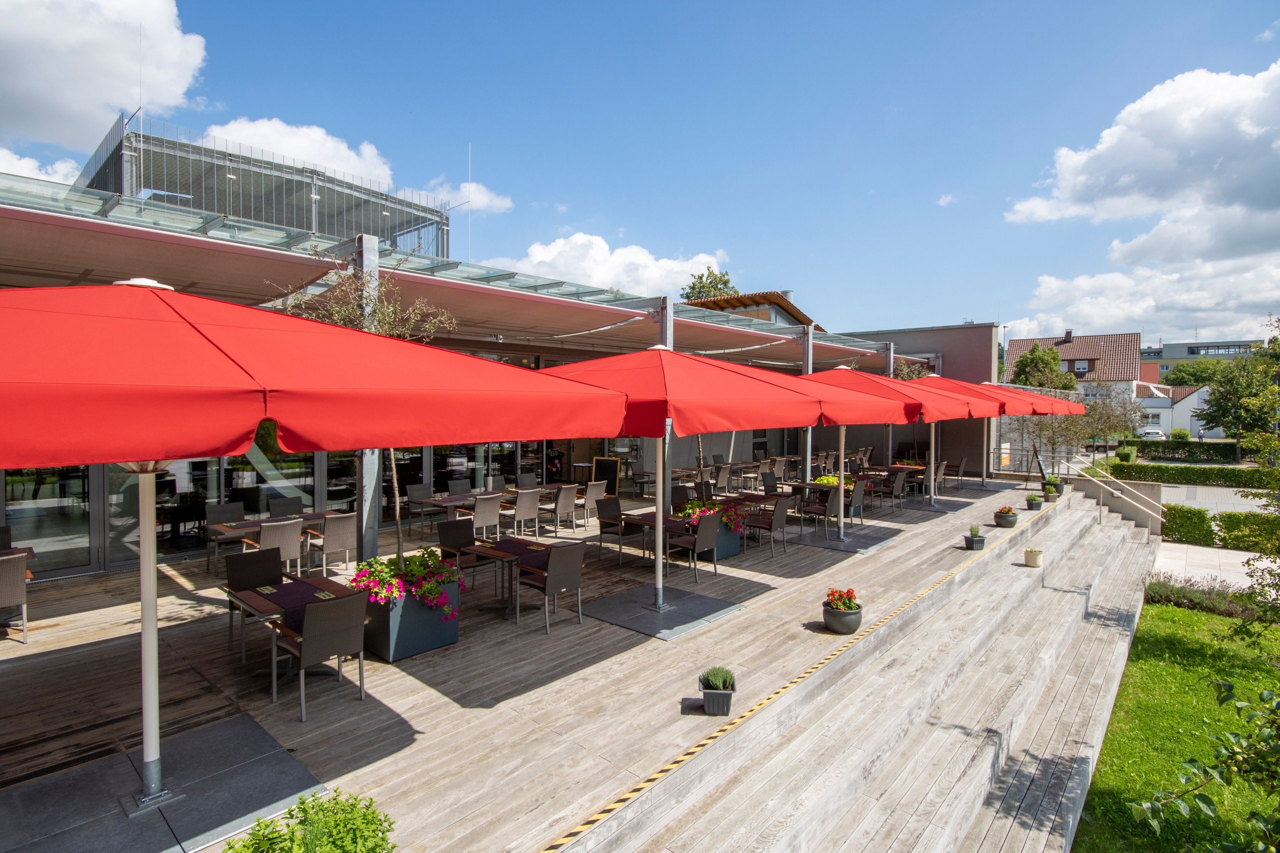 Rote SCHATTELLO-Schirmreihe über der langen Holzterrasse des Restaurants Ropach in Biberach