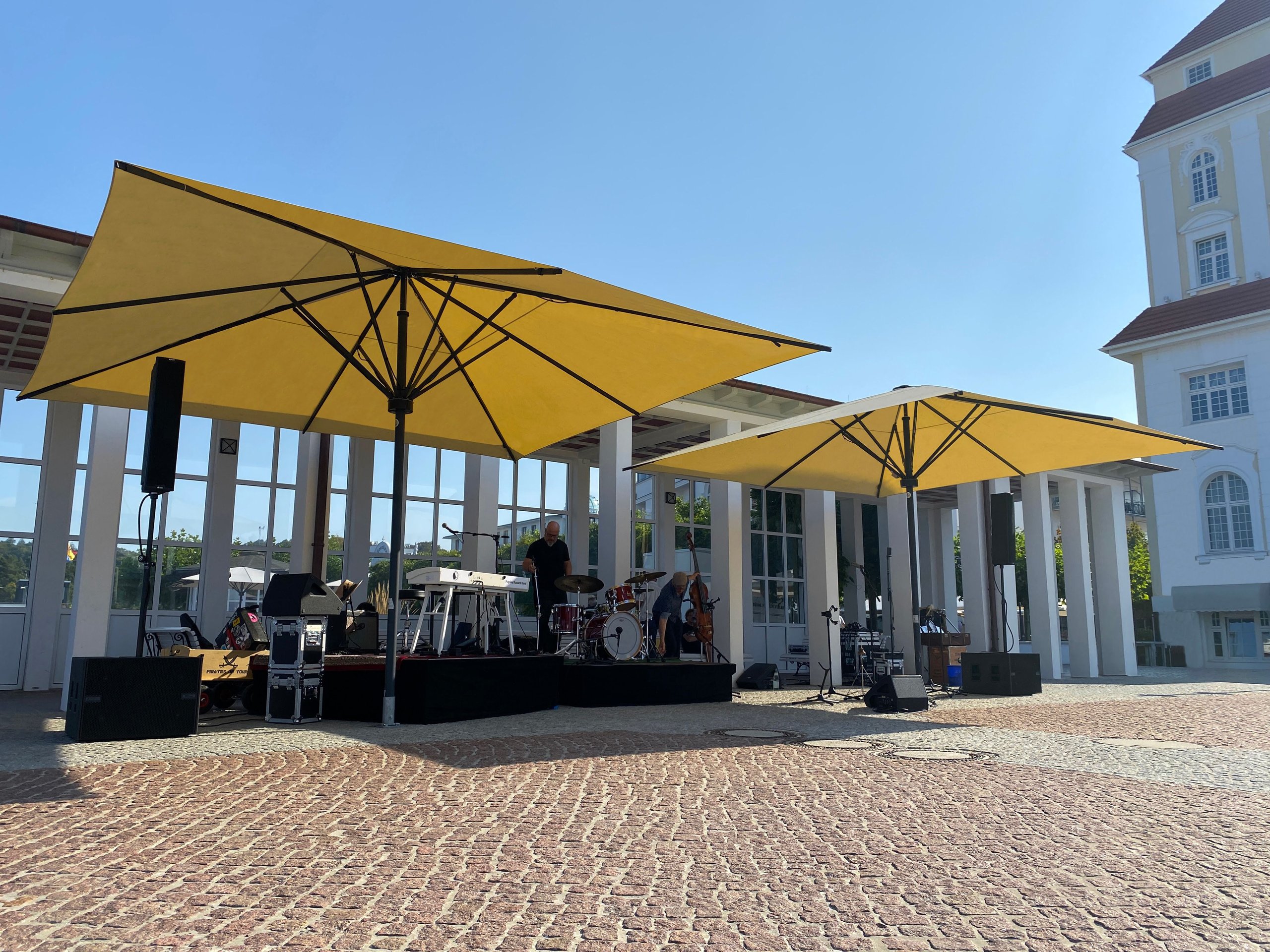 Zwei gelbe SCHATTELLO-Schirme über einer kleinen Bühne auf gepflastertem Platz in Binz