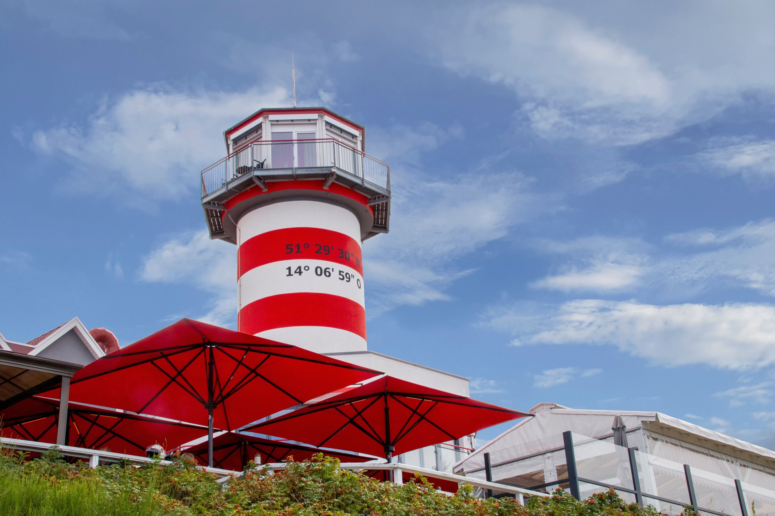 Rote SCHATTELLO-Schirme vor dem rot-weißen Leuchtturm des LeuchtTurm Elsterheide