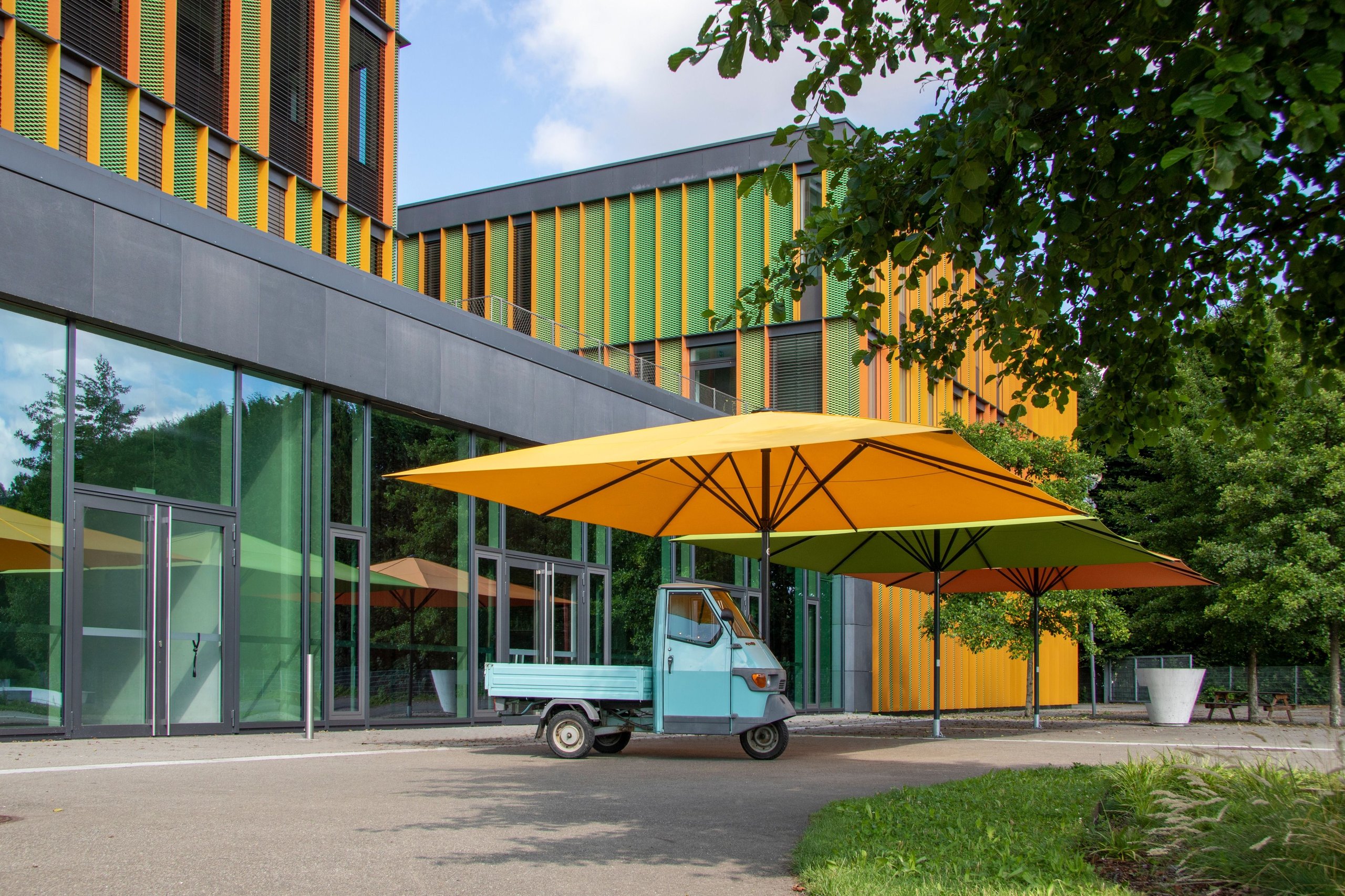 Gelber SCHATTELLO vor der farbigen Fassade der Dollinger Realschule in Biberach