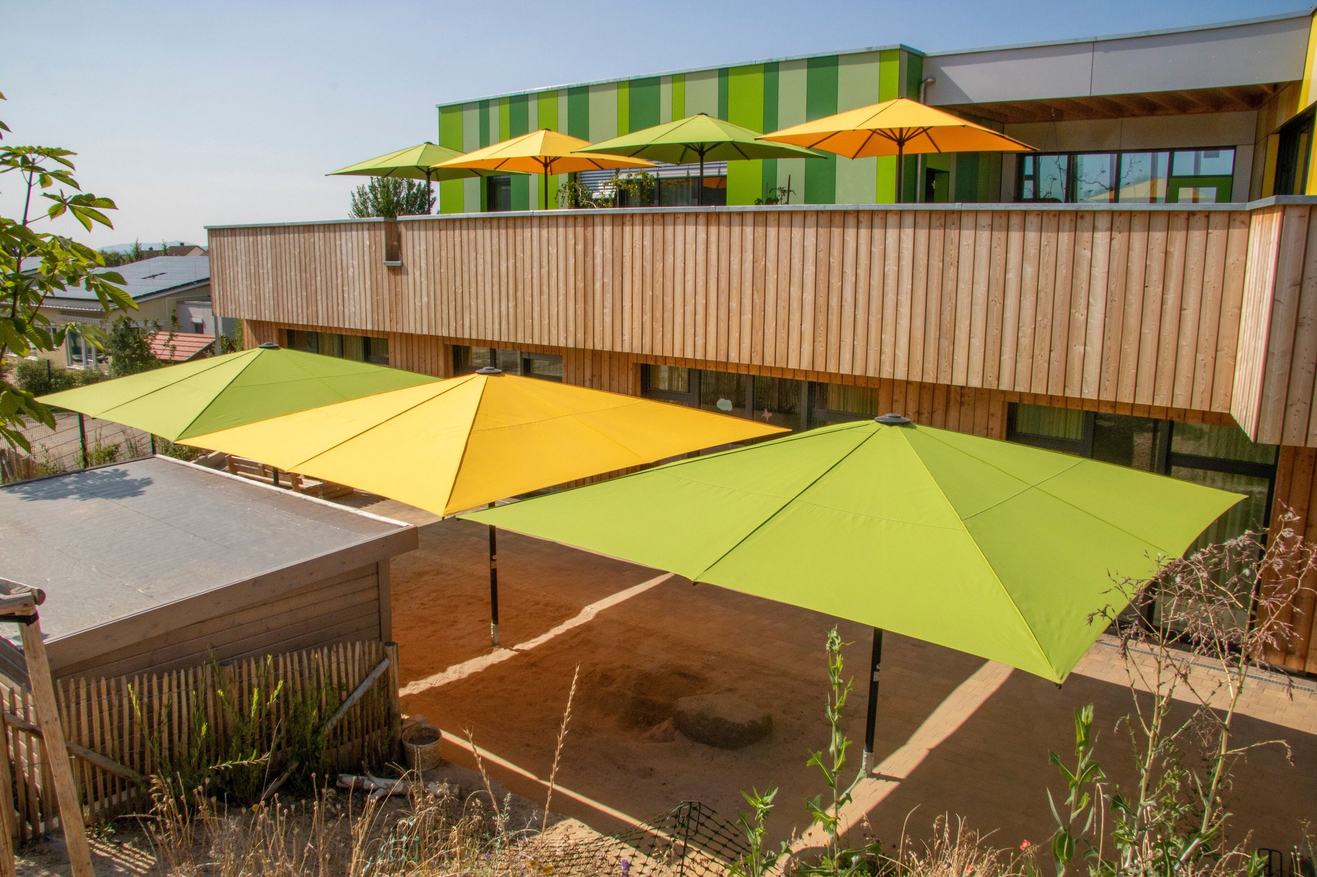 Gelbe und grüne SCHATTELLO-Schirme am Holzbau des Kinderhaus Lauerbäumle in Marbach am Neckar