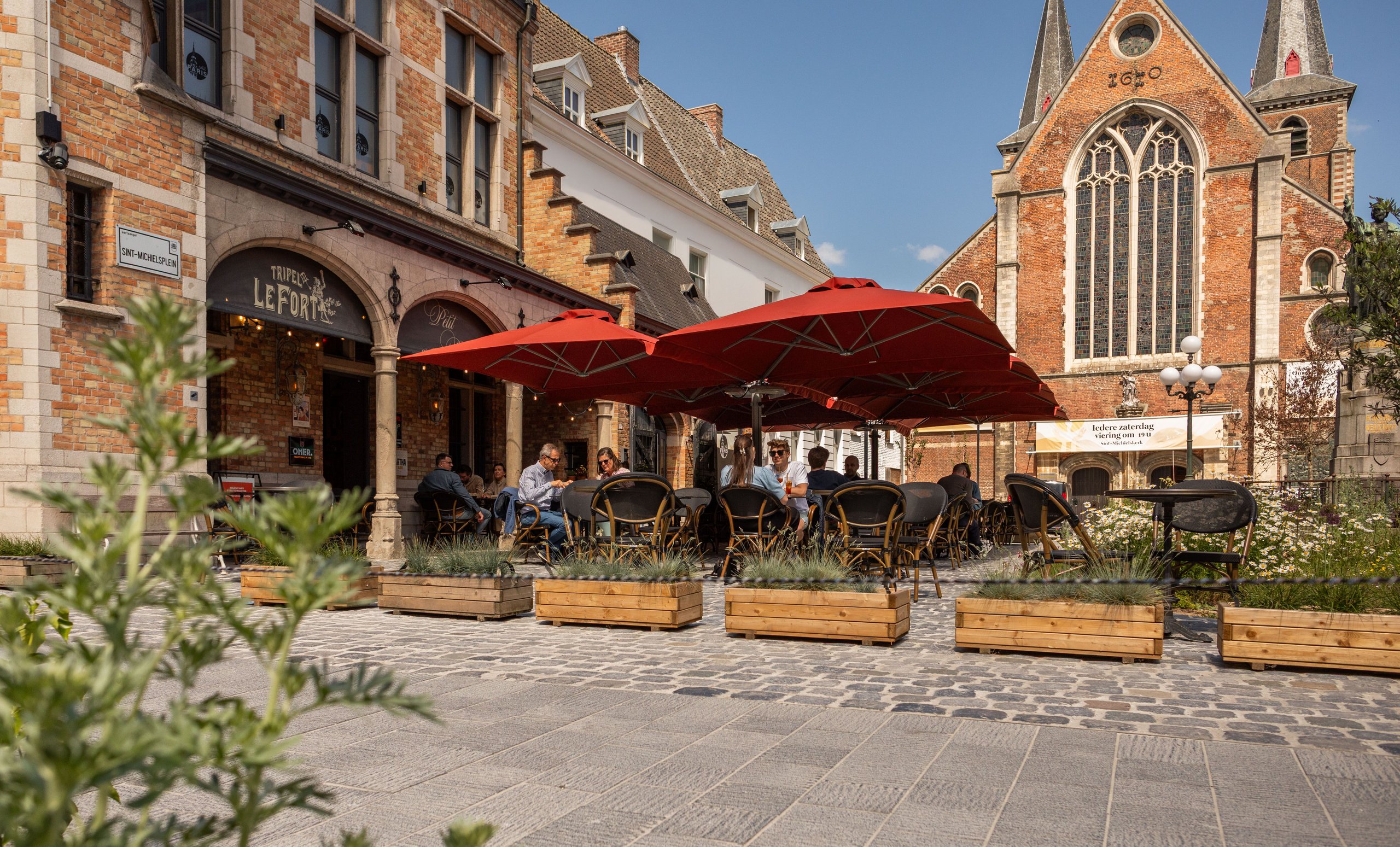 Prostor P6 in Rot über einem Straßencafé vor historischer Backsteinfassade und Kirche