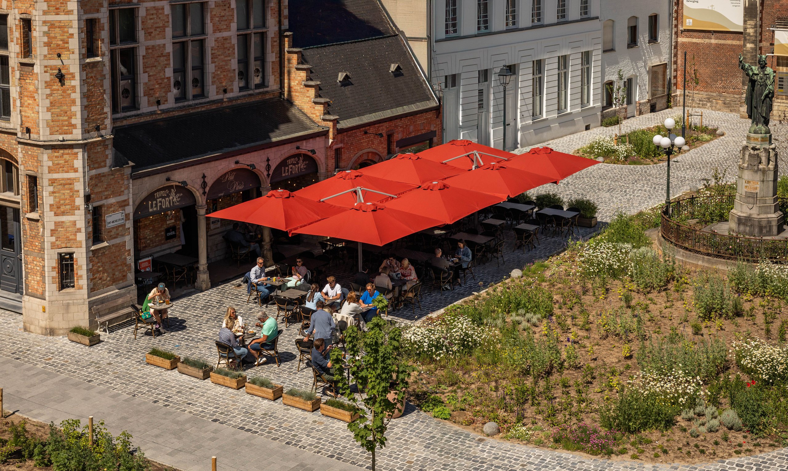 Rote Prostor P6 über den Tischen eines Café-Außenbereichs auf einem Altstadtplatz