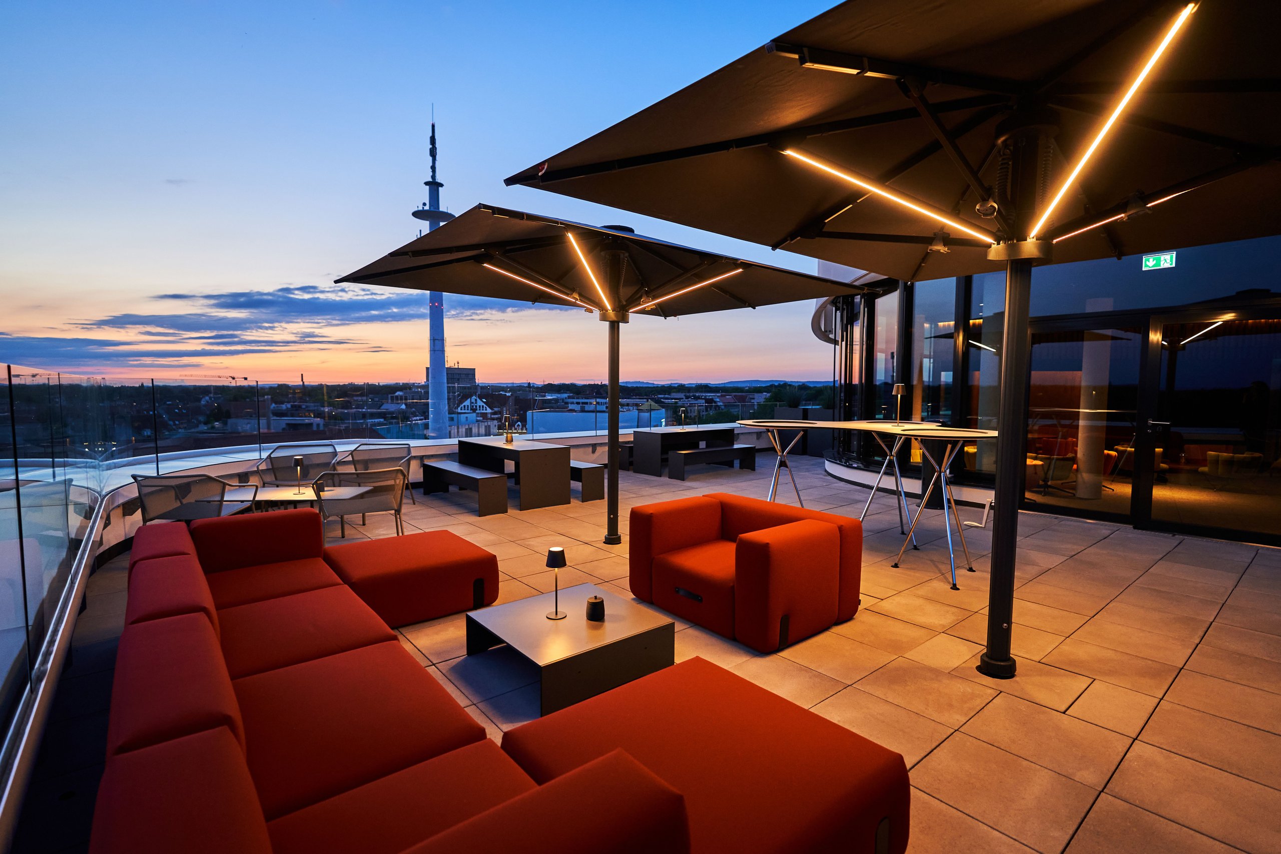 Beleuchtete Glatz Großschirme über einer Rooftop-Lounge zur blauen Stunde