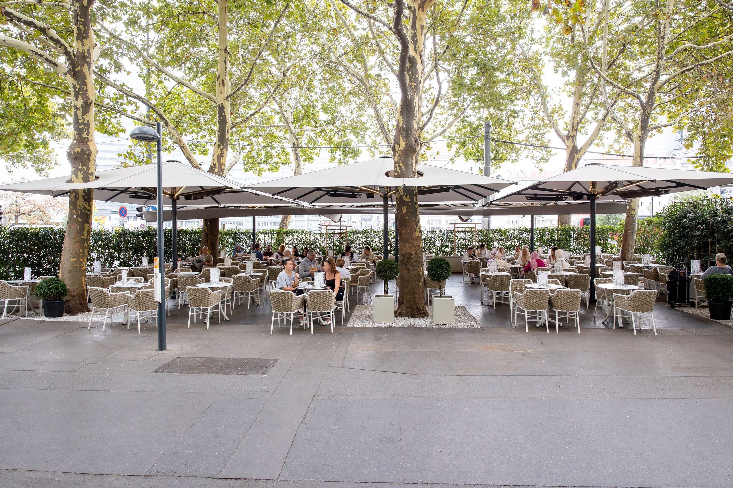 Gekuppelte Glatz Großschirme beschatten eine große Gastronomie-Terrasse unter Platanen