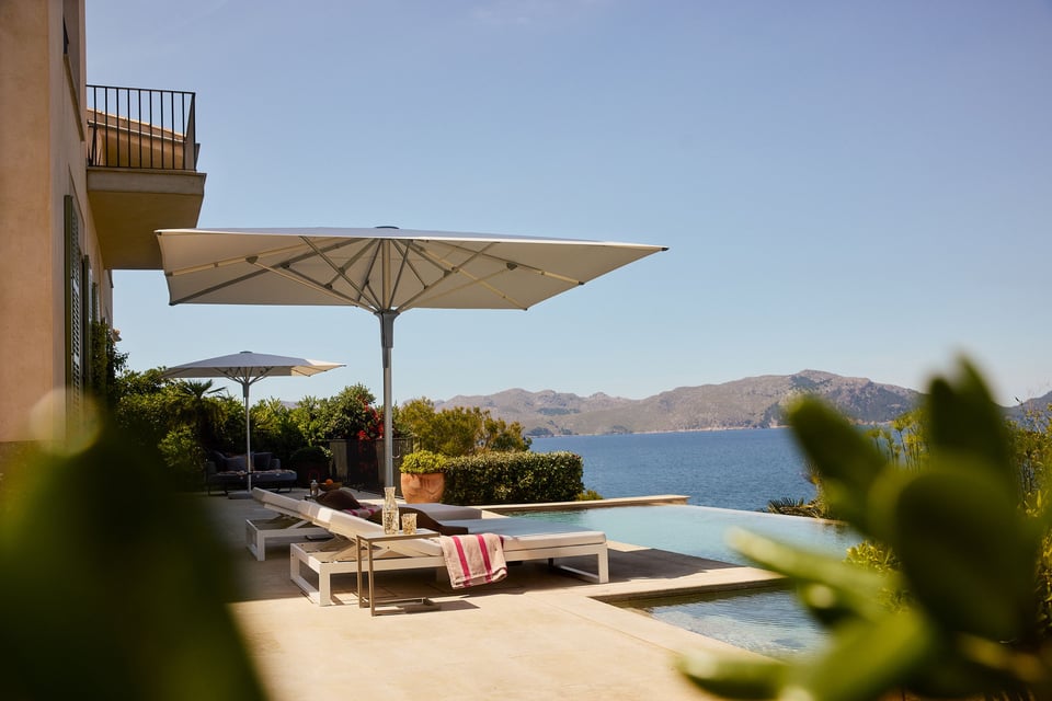 Zwei Glatz Fortello auf einer Terrasse über einer Bucht, Liegen am Infinity-Pool, geöffnete Schirmdächer im Sonnenlicht