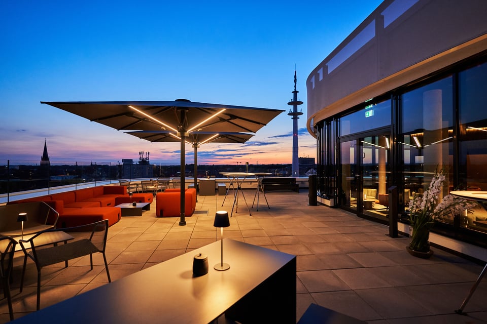 Beleuchteter Glatz Palazzo Noblesse Großschirm über einer Rooftop-Lounge mit roten Sofas am Abend