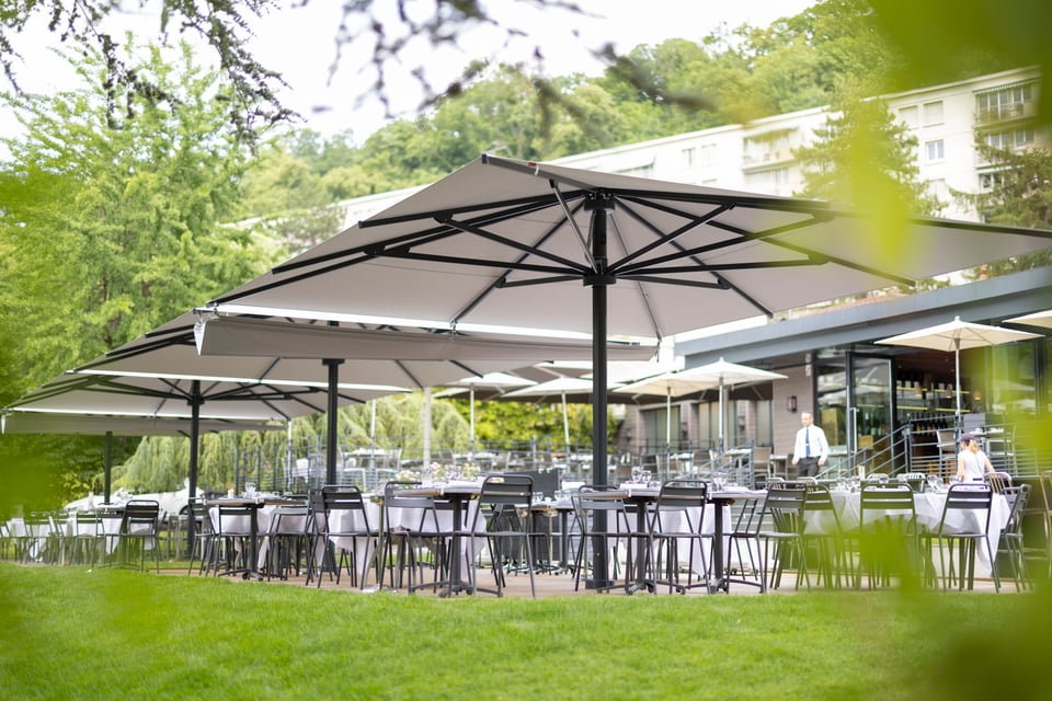 Mehrere großformatige Mittelstockschirme über einer gastronomischen Gartenterrasse mit gedeckten Tischen