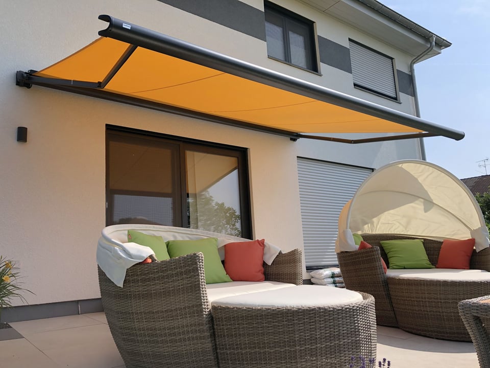 markilux 990 Halbkassettenmarkise mit orangefarbenem Tuch über der Terrasse eines Wohnhauses