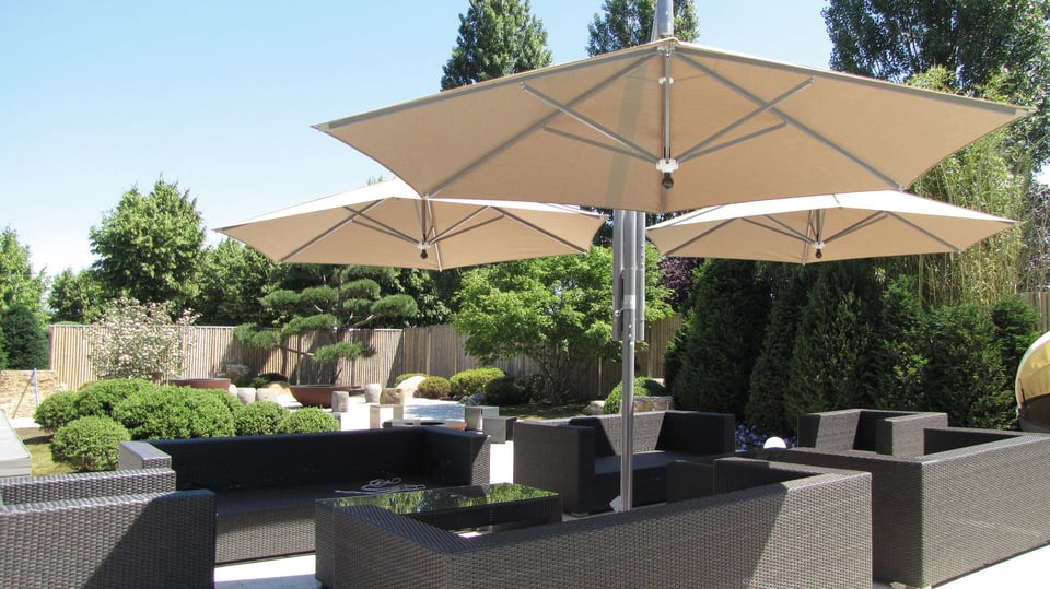 Mehrere gekoppelte RIALTO-Freiarmschirme mit olivebraunen Schirmdächern ohne Volant über einer Garten-Loungeterrasse